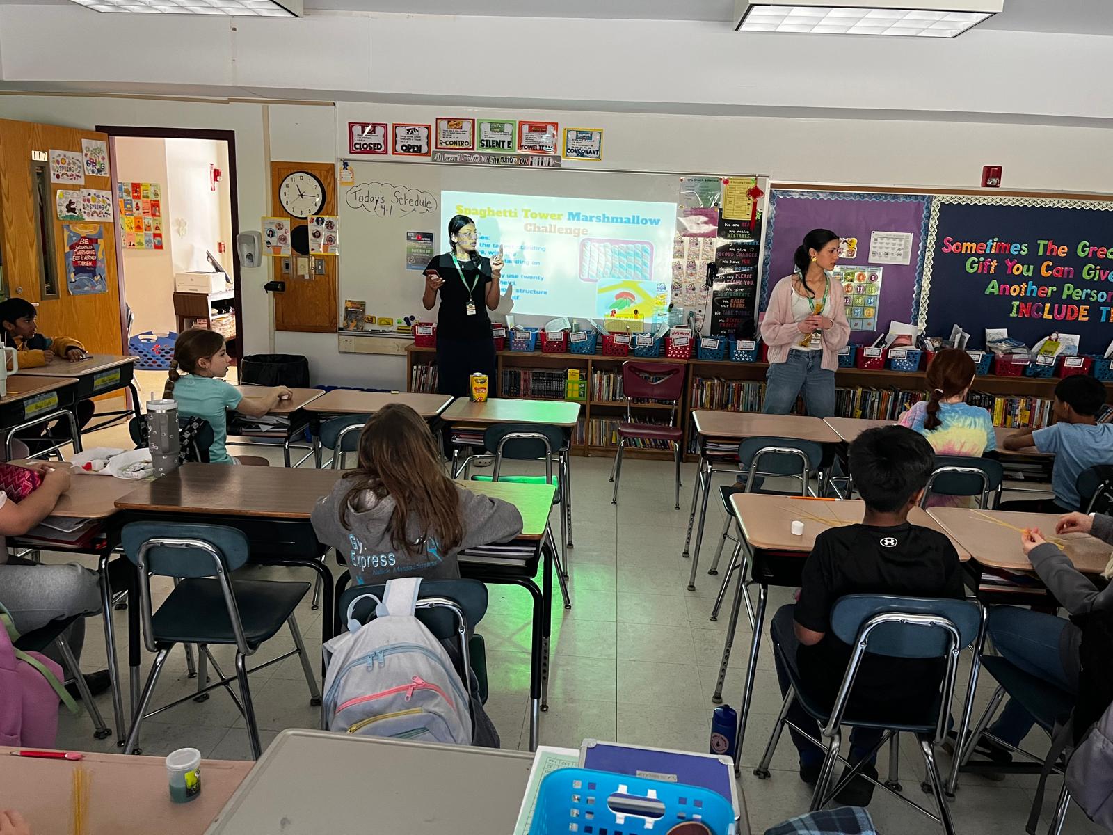 Our student instructors presenting the Spaghetti Tower Marshmallow Challenge to engaged elementary students in a classroom setting